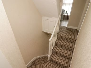 A staircase with striped carpet leading to a hallway with a sink and a small table at Morva in New Quay