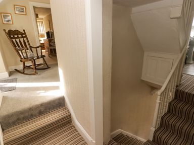 A hallway with striped carpeted stairs leading down and a wooden rocking chair in a carpeted room at Morva in New Quay