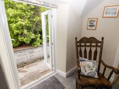 A corner with a wooden chair and a cushion next to an open door leading outside with green plants visible at Morva in New Quay
