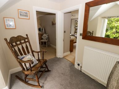A wooden rocking chair with a cushion near two doorways and a large mirror above a radiator at Morva in New Quay