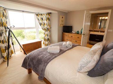 A bedroom with a bed folded towels a wooden chest near the window a telescope and a dresser with a TV at Morva in New Quay