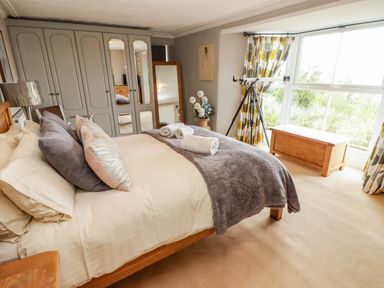 A bedroom with a bed pillows and blankets wardrobe mirror telescope and chest by a window at Morva in New Quay