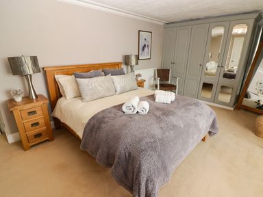 A bedroom with a wooden bed with pillows and folded towels on a grey blanket two bedside tables with lamps a chair a wardrobe with mirrors and a full length mirror at Morva in New Quay