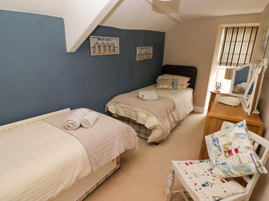 A bedroom with two single beds a wooden dresser with a mirror and a chair with cushions at Morva in New Quay