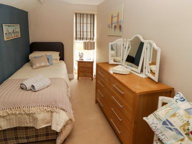 A bedroom with a single bed a wooden chest of drawers with a three-panel mirror a bedside table with a lamp and window blinds at Morva in New Quay