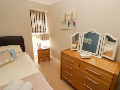 A bedroom with a bed, pillows, bedside table with lamp, wooden dresser with mirror and wall painting at Morva in New Quay