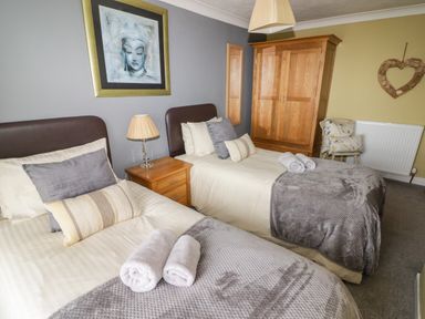 A bedroom with two single beds bedside table lamp wooden wardrobe and a chair at Morva in New Quay