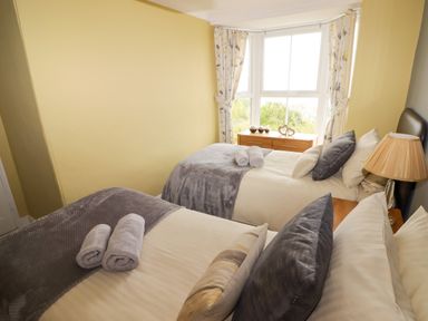 A bedroom with two beds with rolled towels pillows and a lamp near a window at Morva in New Quay