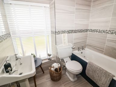A bathroom with a sink soap dispenser a small round table toilet with toilet paper in a basket and a bathtub with a towel at Morva in New Quay
