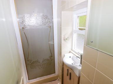 A small bathroom with a shower featuring a frosted glass door and a sink with a cabinet below near a window at Morva in New Quay