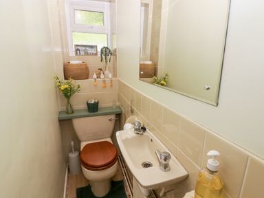 A small bathroom with a toilet, a sink, a mirror, and various decorative items on the windowsill at Morva in New Quay