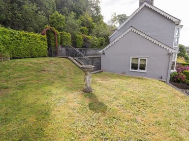 A garden with a birdbath and greenery next to a grey house at Morva in New Quay