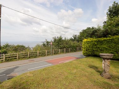 A road with a 30 speed limit sign next to a grassy area with a stone birdbath and bushes at Morva in New Quay