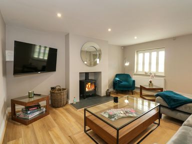 A living room with a wall-mounted TV a fireplace with a round mirror a blue armchair wooden tables and a glass coffee table at Daisy's Place South Creake near Little Walsingham