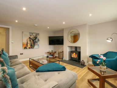 A living room with a gray sectional sofa teal pillows a glass coffee table a fireplace and a wall-mounted television at Daisys Place in South Creake near Little Walsingham