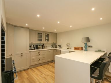 A kitchen with gray cabinets a white countertop a sink a stove bar stools and wooden flooring at Daisys Place in South Creake near Little Walsingham