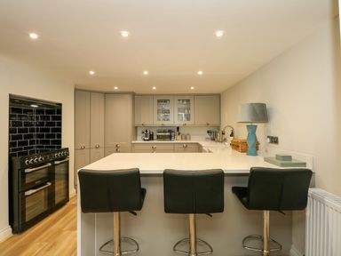 A kitchen with three black bar stools at a white island and grey cabinets at Daisys Place in South Creake near Little Walsingham