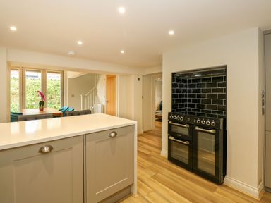 A kitchen with a black stove and oven unit with black tiled backsplash and a countertop island with cabinet storage at Daisy's Place in South Creake near Little Walsingham