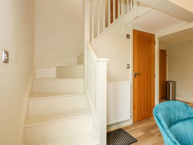A staircase with white steps and railing next to wooden doors and a teal chair at Daisys Place in South Creake near Little Walsingham