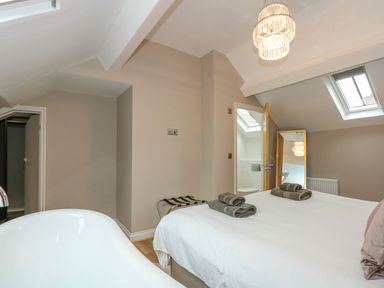 A bedroom with a bed folded towels a large bathtub a doorway to a bathroom and skylight windows at Daisys Place South Creake near Little Walsingham