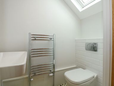 A bathroom with a wall-mounted sink a chrome towel rack a toilet under a skylight at Daisys Place in South Creake near Little Walsingham