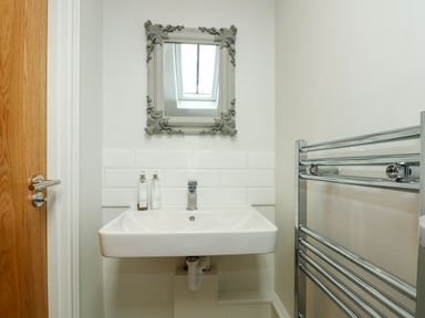 A bathroom sink with two bottles and a decorative mirror above and a chrome towel rack to the side at Daisys Place in South Creake near Little Walsingham