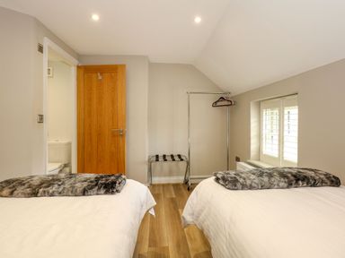A bedroom with two beds a wooden door an open bathroom door a luggage rack a clothes rack with hangers and a window with shutters at Daisys Place in South Creake near Little Walsingham