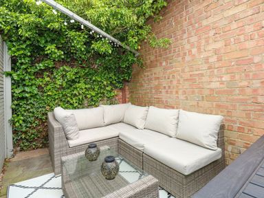 An outdoor seating area with a wicker corner sofa and glass coffee table near a brick wall and a green ivy wall at Daisys Place South Creake near Little Walsingham
