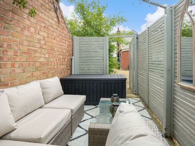 An outdoor seating area with cushioned wicker sofas a glass coffee table a black storage box and light gray wooden fences at Daisys Place South Creake near Little Walsingham