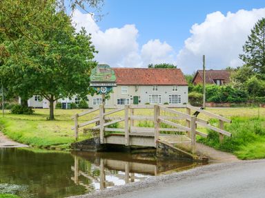 A small wooden bridge over a waterway with a South Creake village sign and houses in the background at Daisys Place in South Creake near Little Walsingham