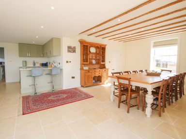 A dining area with a wooden table and chairs next to a kitchen counter with two bar stools and a wooden cabinet at Daniels Farmhouse in Claines