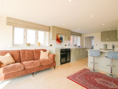 A kitchen with green cabinets a stove a red patterned rug and a brown sofa with pillows at Daniels Farmhouse in Claines
