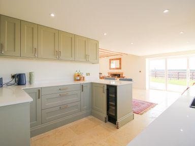 A kitchen with cabinets and a countertop opening to a dining area and a sliding glass door with a view outside at Daniels Farmhouse in Claines