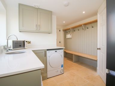 A utility room with a sink microwave washing machine wooden bench and wall hooks at Daniels Farmhouse in Claines