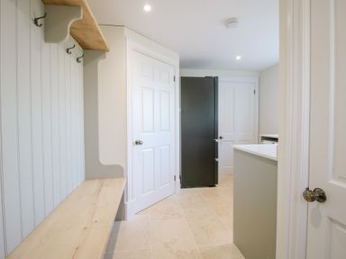 A utility room with a black refrigerator two white doors a wooden bench with hooks and tiled floor at Daniels Farmhouse in Claines