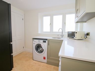 A kitchen with a washing machine under the counter a sink near three windows and a microwave on the countertop at Daniels Farmhouse in Claines
