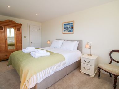 A bedroom with a bed with white linens and green blanket beside a white nightstand and wooden wardrobe at Daniels Farmhouse in Claines