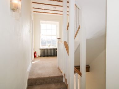 A hallway with carpeted stairs wooden railing a window with a radiator below and a fire extinguisher at Daniels Farmhouse in Claines