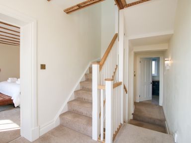 A hallway with carpeted stairs leading up and down and a bedroom visible through an open door at Daniels Farmhouse in Claines