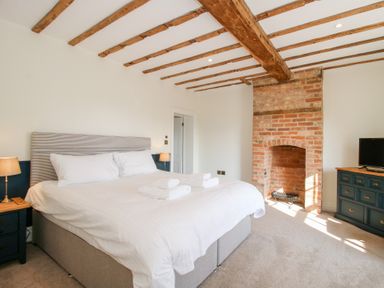 A bedroom with a large bed two bedside tables with lamps a brick fireplace and a dresser with a television at Daniels Farmhouse in Claines