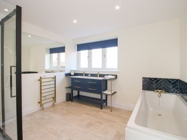 A bathroom with a bathtub a double sink vanity with mirror towel rack and window at Daniels Farmhouse in Claines