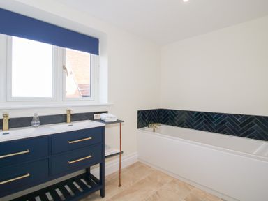 A bathroom with a blue vanity unit with two sinks and a bathtub with dark tiles at Daniels Farmhouse in Claines