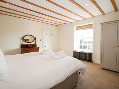 A bedroom with a bed towels on it a wooden dresser with mirror a wardrobe and a window with radiator below at Daniels Farmhouse in Claines