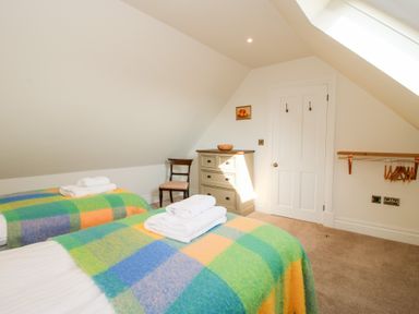 A bedroom with two single beds covered with checkered blankets towels on beds a wooden chair a chest of drawers and a door at Daniels Farmhouse in Claines
