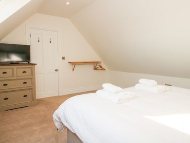 A bedroom with a bed with towels a chest of drawers with a television a door and a shelf with hangers at Daniels Farmhouse in Claines