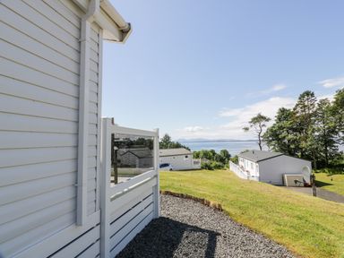 A view of white houses on a grassy hill with trees and water in the background at Bethany's Retreat in Wemyss Bay