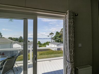 A patio door open to a balcony with chairs and a table overlooking houses trees and water at Bethany's Retreat in Wemyss Bay