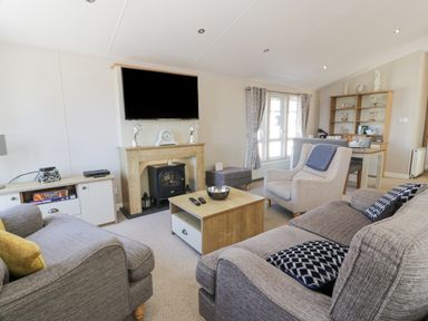 A living room with gray sofas, a flat screen TV above a fireplace, a wooden coffee table, and a dining table with chairs at Bethany's Retreat in Wemyss Bay
