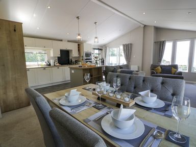An open dining and living area with a set dining table and kitchen in the background at Bethany's Retreat in Wemyss Bay
