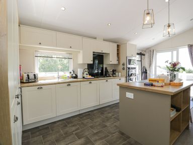 A kitchen with white cabinets, a wooden countertop island, a toaster, a kettle, a gas stove, built-in microwave and oven, and flowers on the island at Bethany's Retreat in Wemyss Bay